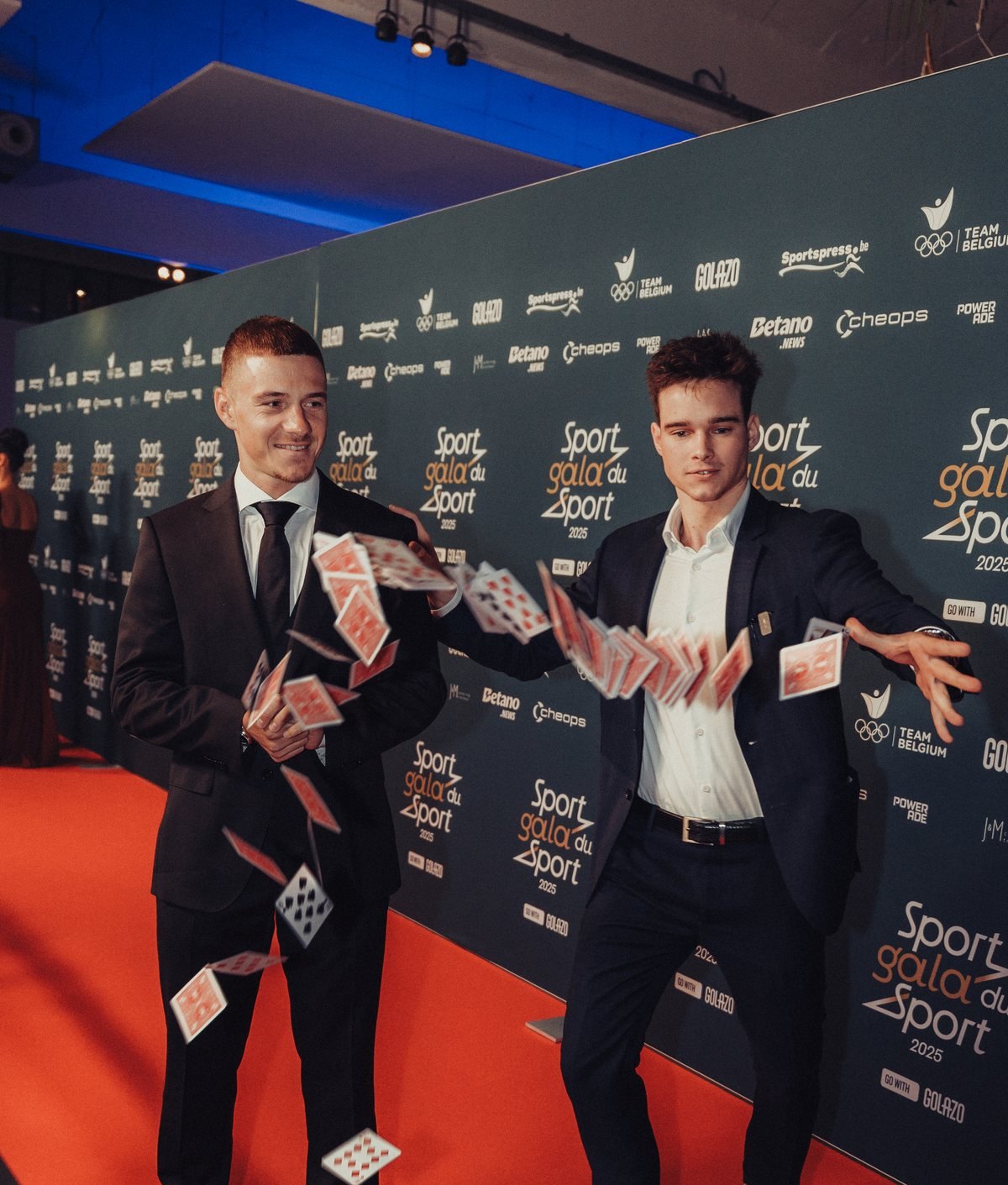 Two guests laughing as playing cards burst into the air on a branded red carpet