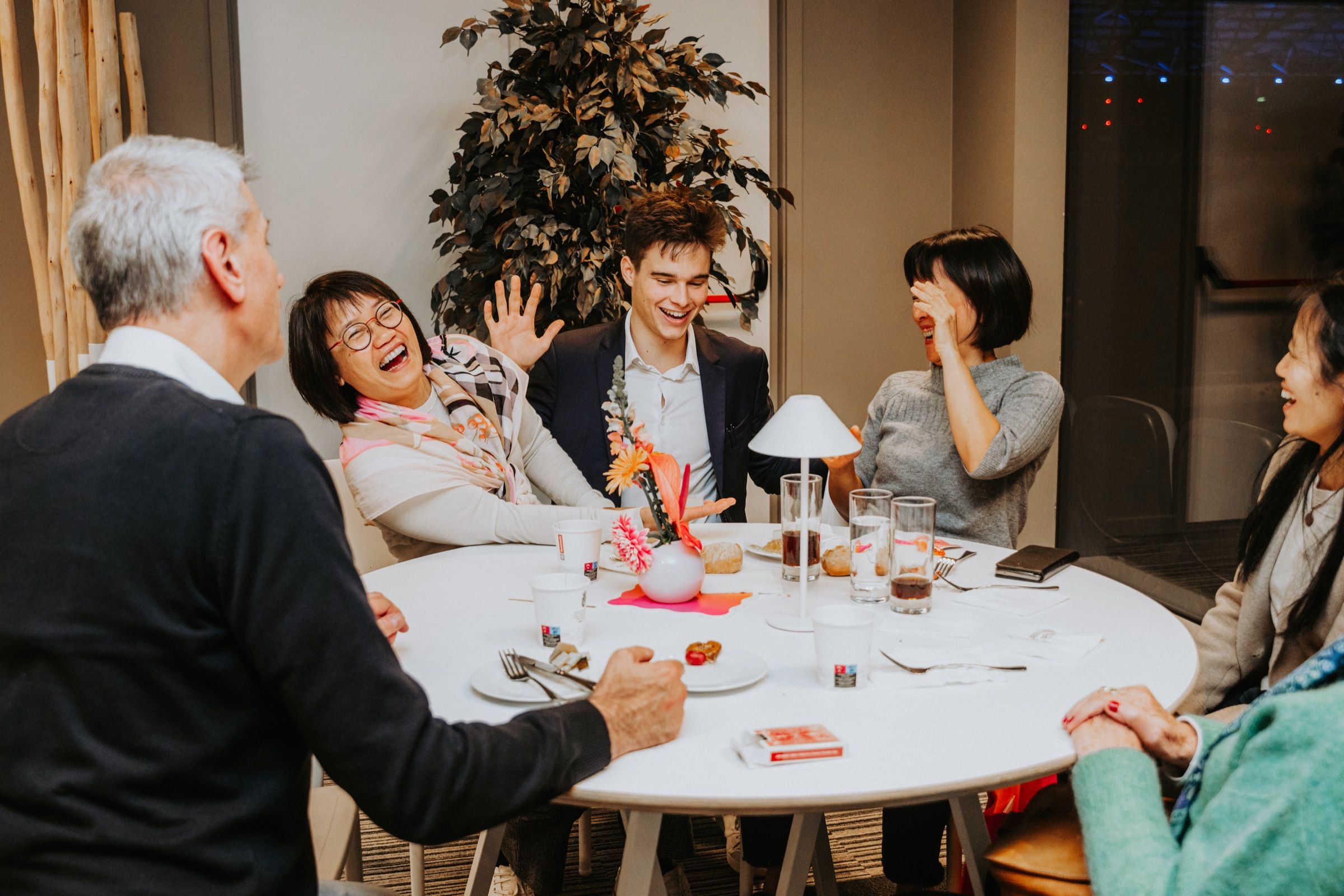 Guests at a family dinner reacting with laughter and surprise to a card reveal