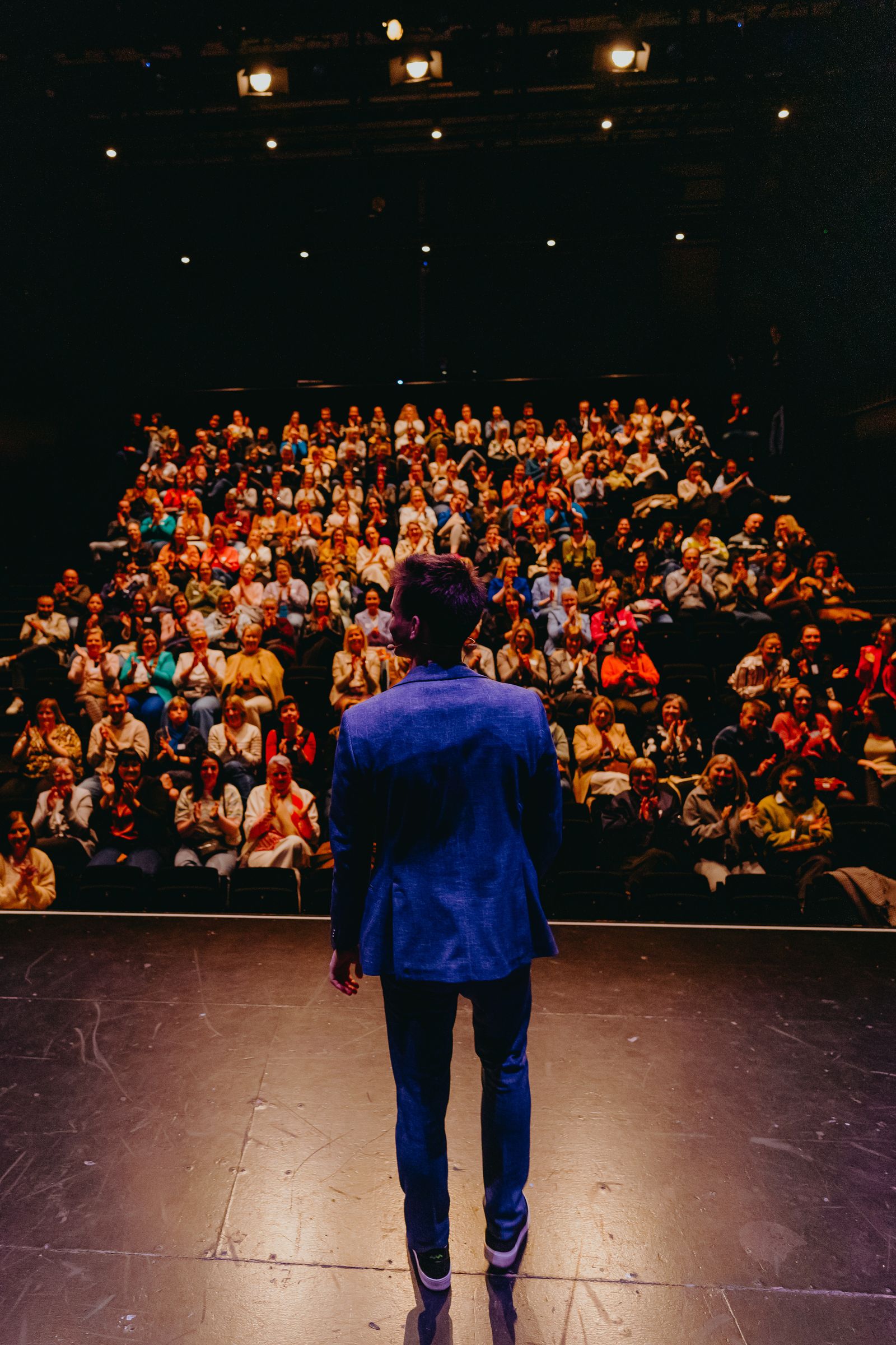 Jonas De Bruyn facing a full theatre audience giving a standing ovation