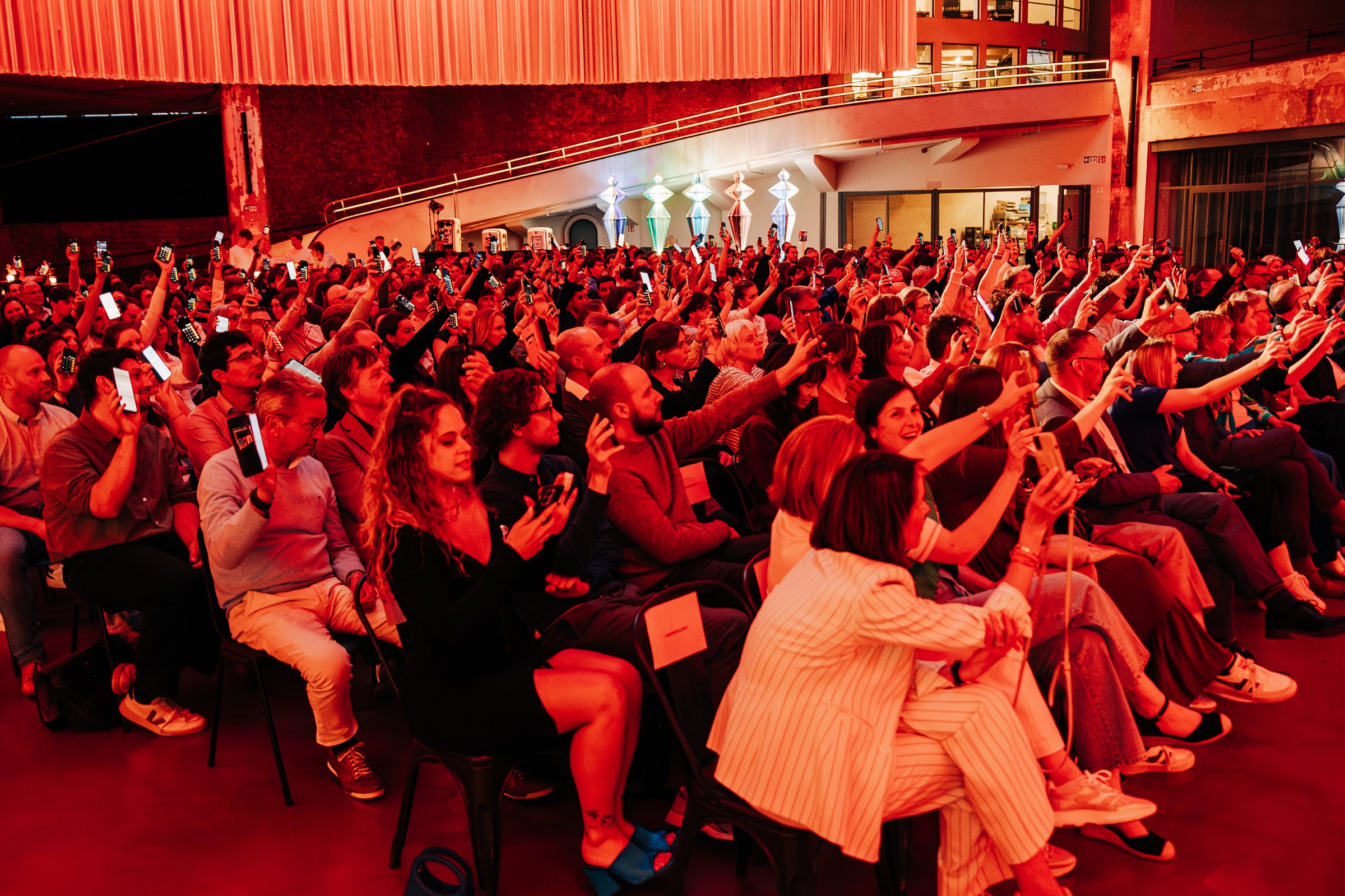 A packed theatre audience holding up phone lights during a performance